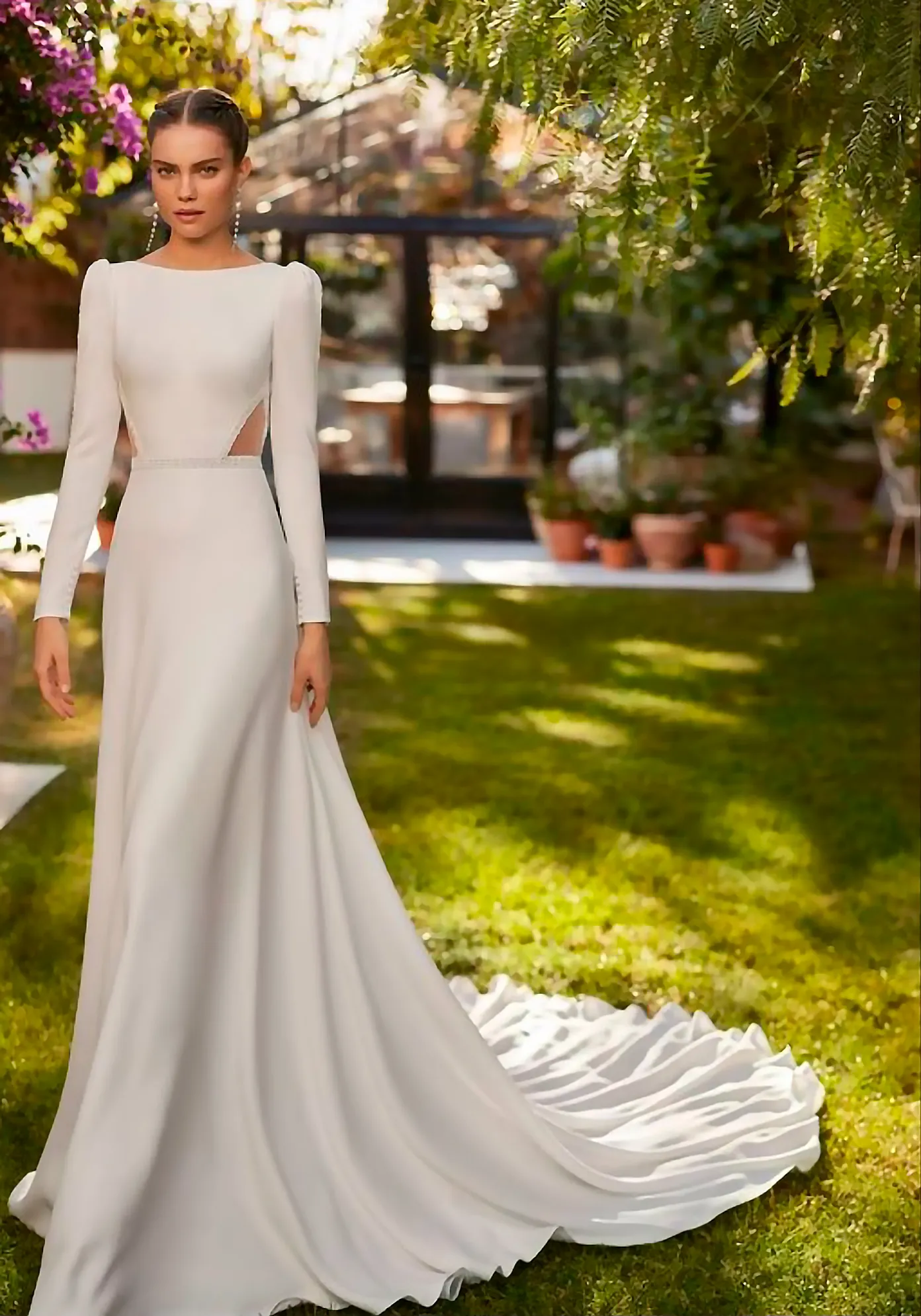 Novia con vestido de manga larga y cola en un jardín